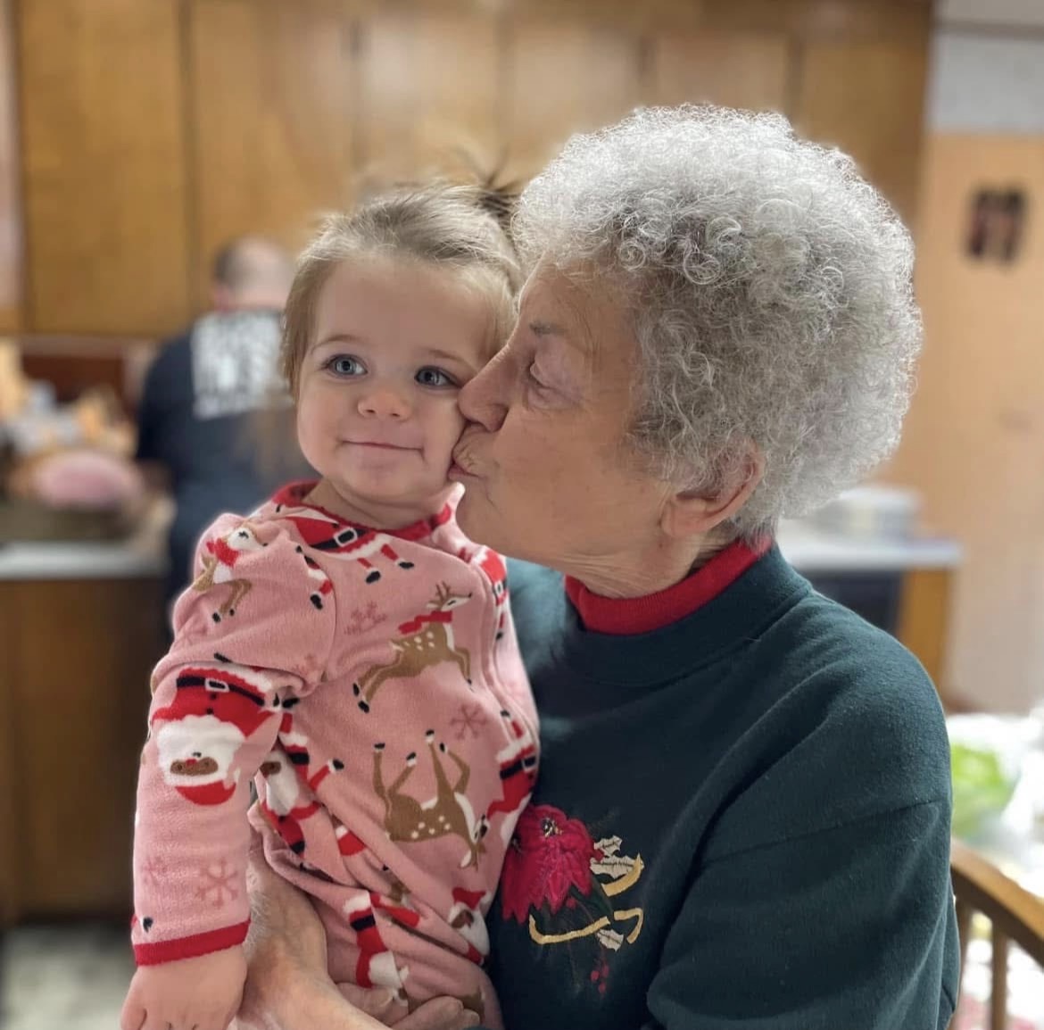 A grandmother kissing her young granddaughter on the cheek at home.